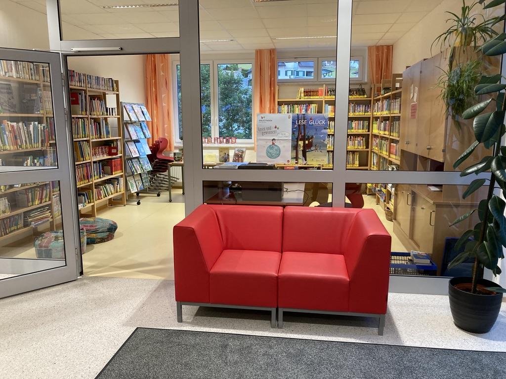 Bücherei von innen - rotes Sofa und dahinter im nächsten Raum Bücherregale